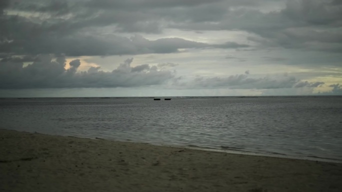 热带岛屿上的沙滩。海浪冲刷着海岸。背景是日落时的乌云。马尔代夫。