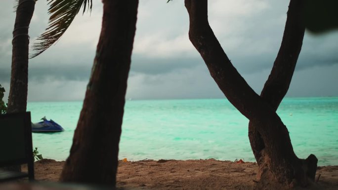 沙滩上的热带棕榈树。在海湾里，一艘水上摩托艇在波浪上滑行，背景是多云的日落天空。马尔代夫。
