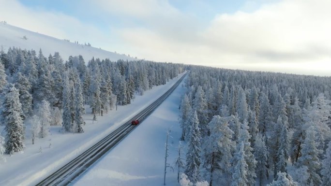 无人机尾随一辆红色电动汽车行驶在冬季拉普兰的雪林中
