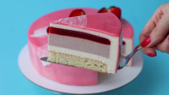 女性的手展示了一块草莓慕斯蛋糕，然后把它移向镜头。粉红色的蛋糕配上蓝色背景的草莓。近距离