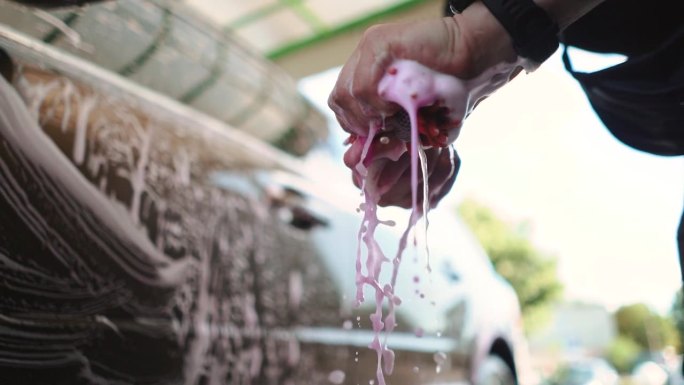 一名男司机在自助洗车店洗车时，正在拧干沾有水和粉色纳米泡沫的毛巾