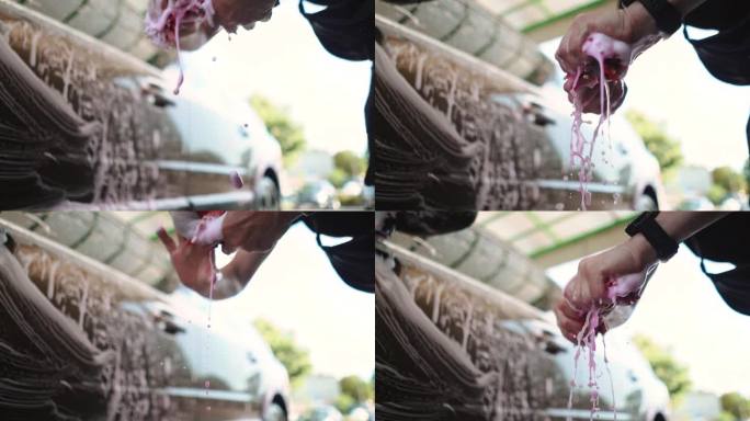 一名男司机在自助洗车店洗车时，正在拧干沾有水和粉色纳米泡沫的毛巾