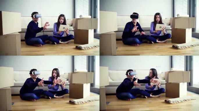一对年轻夫妇带着平板电脑和VR眼镜坐在地板上，搬进了新家。