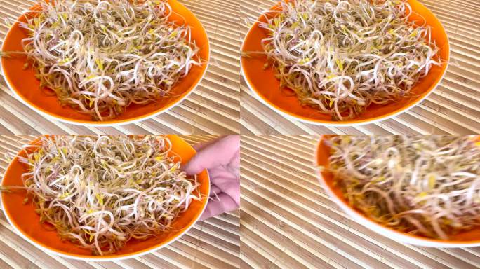 一堆发芽的绿豆，有小根，在竹背景上吃一个橙色碗。厨师的手从桌子上拿走了一个橙色的碗。饮食理念，素食主