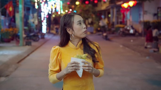 越南妇女穿着传统服装，晚上在会安街上散步和吃当地披萨的慢动作