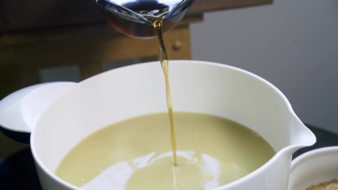 将棕色液体甜味剂倒入盛满新鲜姜根汁的白色碗中