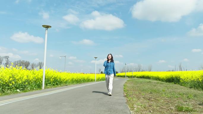 年轻美女走在春天盛开的金黄油菜花海里