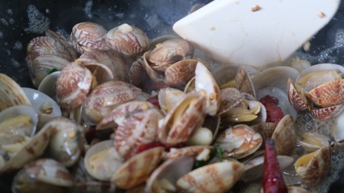 在锅中翻炒蛤蜊，烹饪海鲜菜肴
