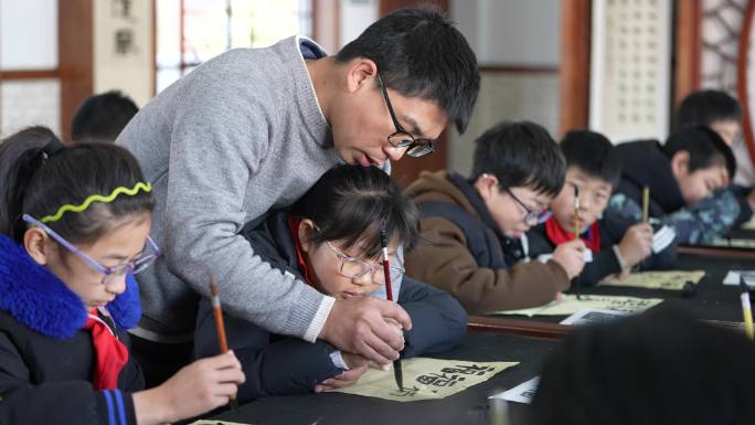 学校书法课老师手把手教小朋友手拿毛笔写字