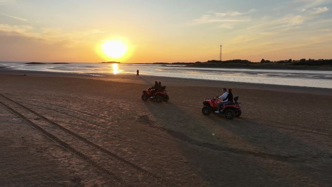 夕阳晚霞中游客在海边沙滩骑沙滩摩托