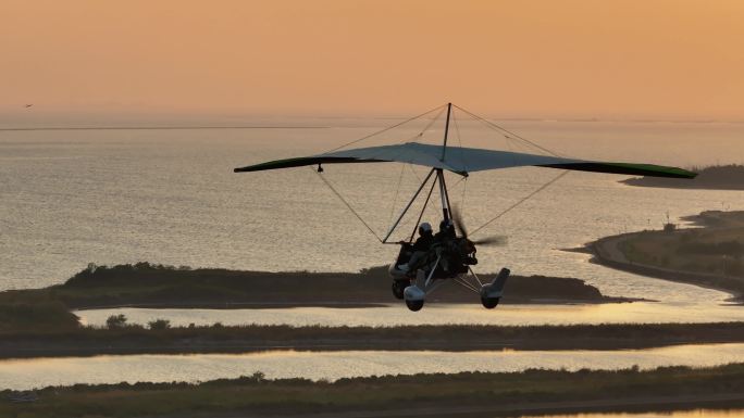 傍晚夕阳晚霞下三角动力滑翔机载乘客飞过海面着陆沙滩
