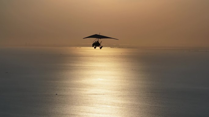 滑翔机在夕阳照射的水面上飞翔