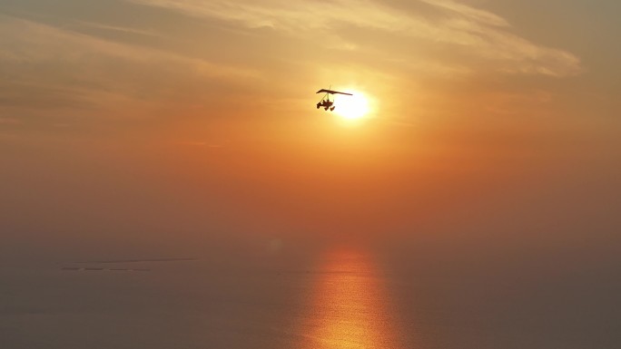 夕阳晚霞红日照射海面水面游客搭载滑翔机飞翔逆光剪影