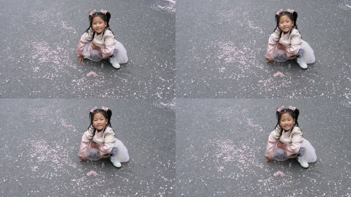 可爱小女孩将地上的樱花花瓣排成爱心形