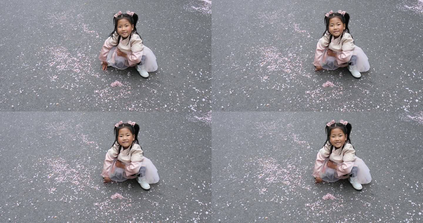 可爱小女孩将地上的樱花花瓣排成爱心形