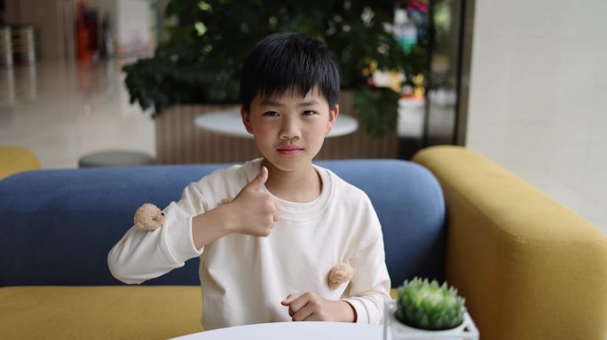可爱的中国小男孩坐在沙发上竖起大拇指