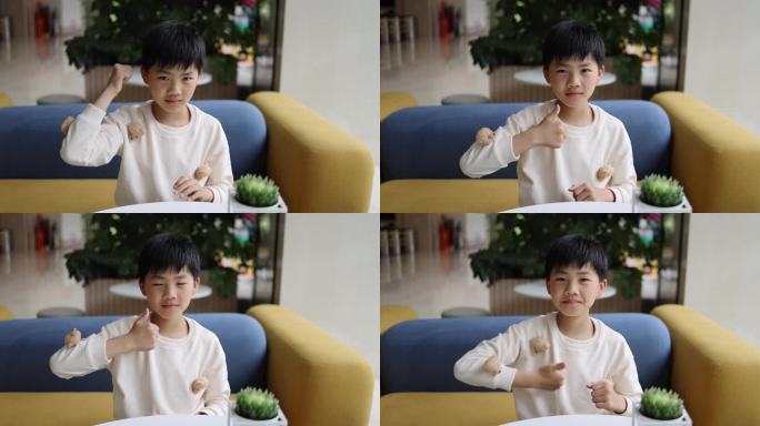 可爱的中国小男孩坐在沙发上竖起大拇指