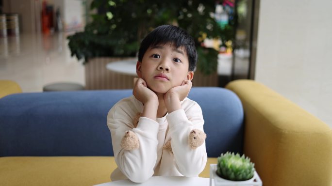可爱的中国小男孩坐在沙发上托腮卖萌