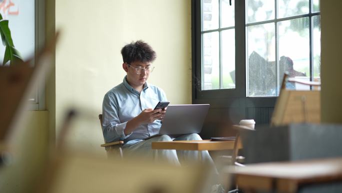 年轻男人在咖啡店使用手机笔记本电脑工作