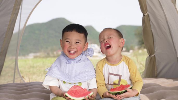 小孩吃西瓜-两个小孩坐在帐篷里吃西瓜嬉笑