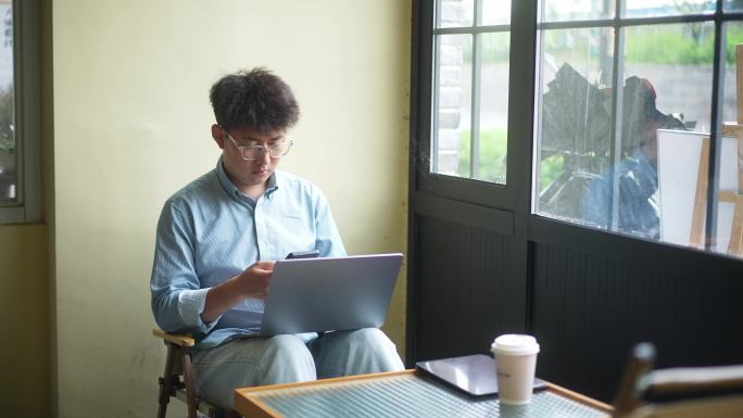年轻男人在咖啡店使用手机笔记本电脑工作