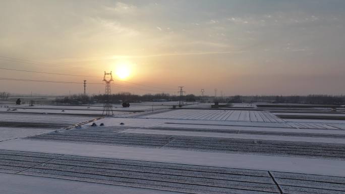 雪后夕阳下的输电塔和村庄