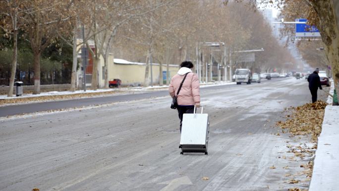 下雪雪地道路泥泞年轻人拉着行李箱赶路背影