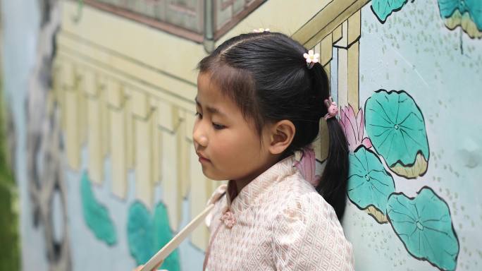 可爱小女孩拿在扇子在古镇涂鸦墙前微笑