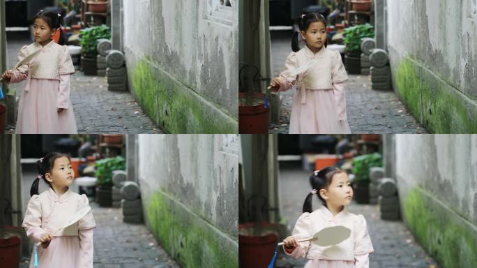 可爱小女孩拿在扇子在古镇小巷里行走