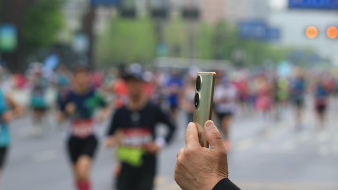 用手机拍摄正在进行的马拉松比赛