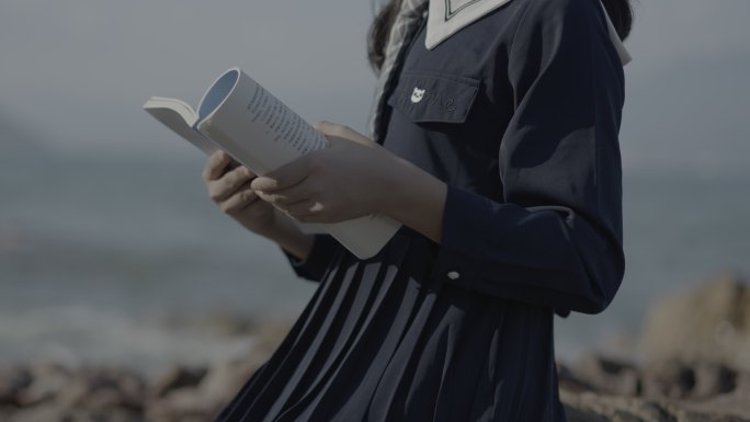 身穿黑色长裙女学生手拿书籍在海边录制歌曲