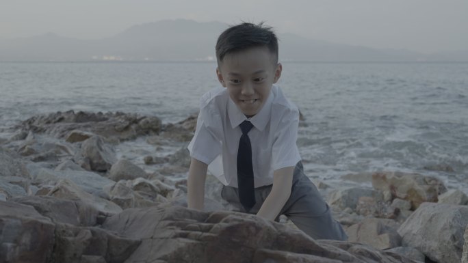 小男孩在海边微笑着勇敢的攀登礁石拍摄MV