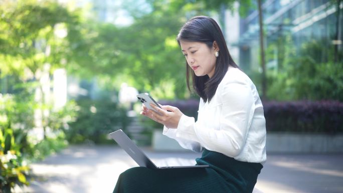 职业女性户外使用笔记本电脑和手机办公