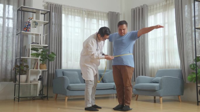 全身的亚洲男医生和一个胖男病人在诊所。病人用称重机量体重，医生用卷尺量腰围