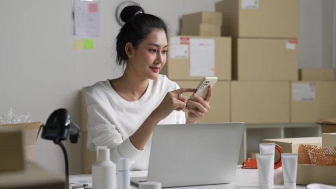 亚洲女卖家在电话中确认客户的订单。在仓库工作的电子商务企业主。
