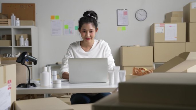 亚洲女网上卖家在笔记本电脑上确认顾客的订单。在仓库工作的电子商务企业主。