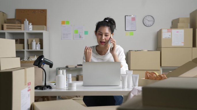 亚洲女卖家在电话中确认客户的订单。在仓库工作的电子商务企业主。