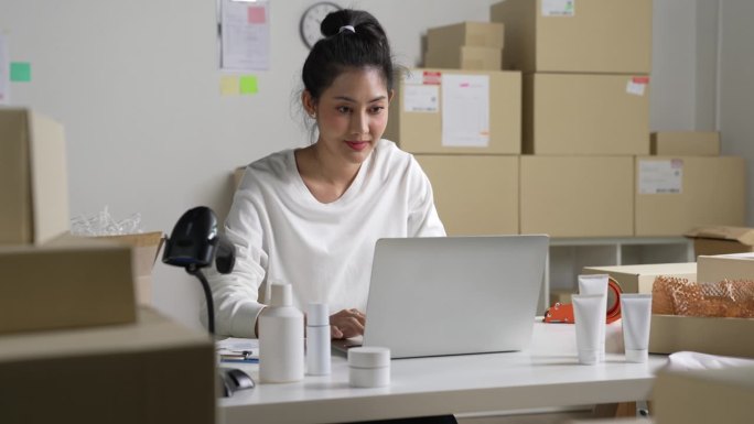 亚洲女网上卖家在笔记本电脑上确认顾客的订单。在仓库工作的电子商务企业主。