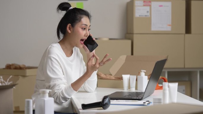 亚洲女卖家在电话中确认客户的订单。在仓库工作的电子商务企业主。