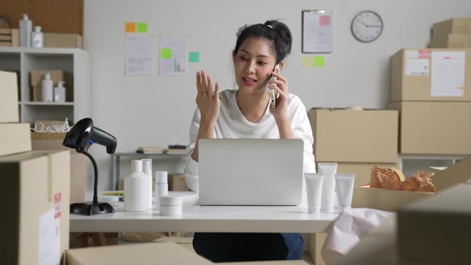 亚洲女卖家在电话中确认客户的订单。在仓库工作的电子商务企业主。