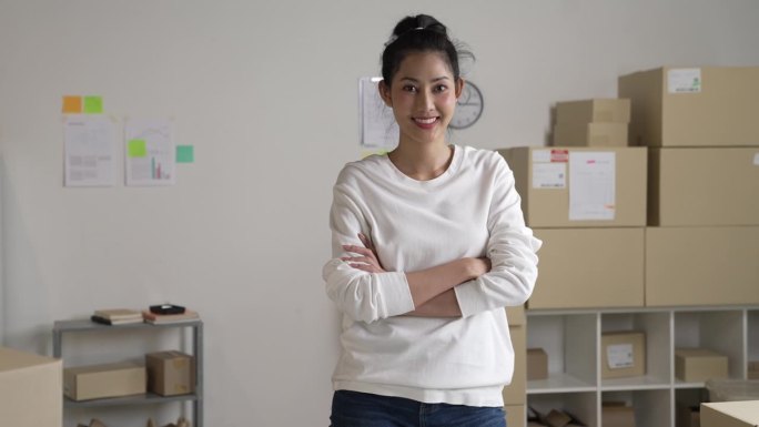 自信的年轻亚洲女性零售商，企业家，在线商店dropshipping小企业主站在配送仓库里拿着包裹箱看