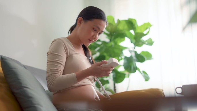 亚洲孕妇用袖珍多普勒聆听婴儿的心跳，露出快乐的微笑。