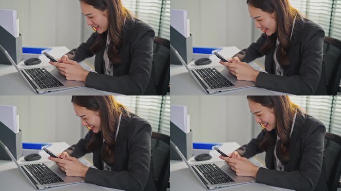 亚洲快乐女商人在办公室工作时刷智能手机。在公司工作场所，穿着正装坐在办公桌上用手机搜索社交媒体的漂亮