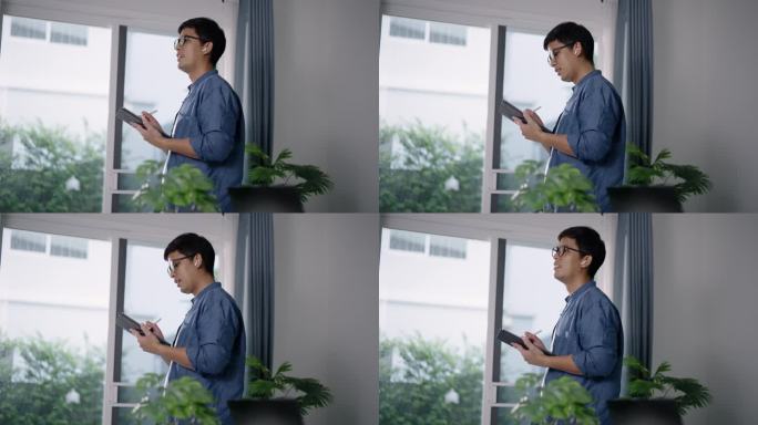 亚洲男人早上在家办公室喝着咖啡，放松地用平板电脑上的人工智能来更新任务工作。