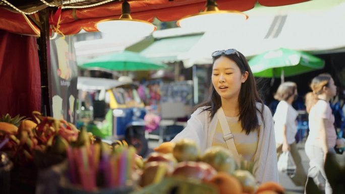 在曼谷度假期间，一名年轻女子正在一个街头市场买水果。