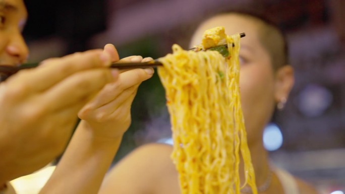 晚上吃街头小吃的年轻夫妇用筷子夹起冬阴凉面，舀进碗里。