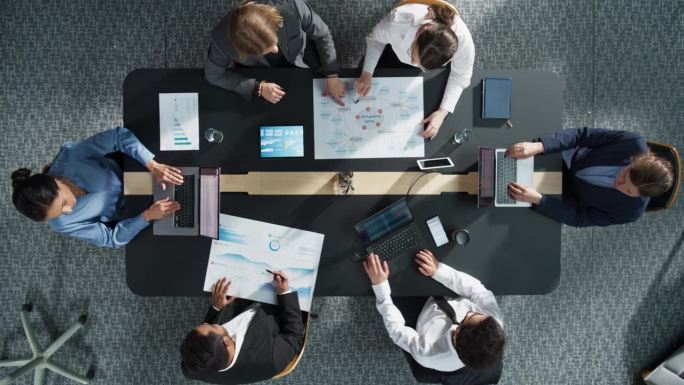 自上而下的视图，缩小:不同的专业人士在一个办公室工作的业务统计报告和数字计划。用笔记本电脑和图表进行