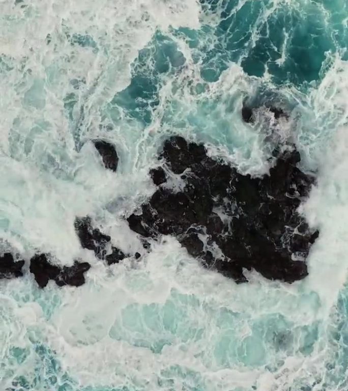 带着白色泡沫的海浪拍打着岩石。从空中俯瞰暴风雨的海浪。海或海浪飞溅，竖屏