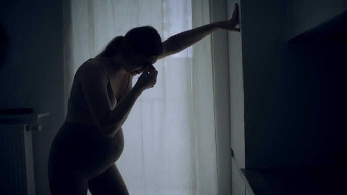 孕妇临产的剪影。她疼了，摸了摸肚子。
