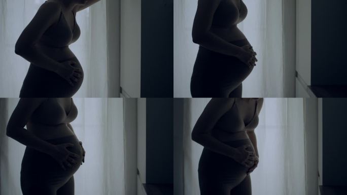 孕妇临产的剪影。她疼了，摸了摸肚子。